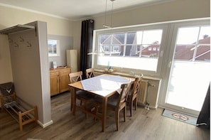 A room with a dining table, chairs, a radiator, a window with a view, and a coat rack. - Holiday apartment in Greetsiel with Wi-Fi (Greetsiel)