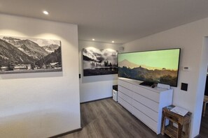 A modern living room with a flat-screen TV, a white entertainment unit, and two framed landscape photographs on the wall. - Holiday apartment with 1 bedroom (Oberstdorf)
