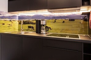 A kitchen with a built-in coffee maker, a sink, and a view of a green field with cows. - Holiday apartment with 1 bedroom (Oberstdorf)