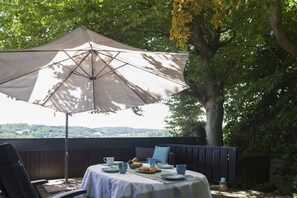 Eine Terrasse im Freien mit einem Tisch für zwei Personen, einem großen Sonnenschirm und Blick auf die Landschaft.
