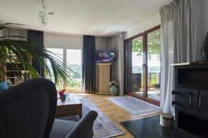 Ein modernes Wohnzimmer mit Fernseher, einer Couch, einem Couchtisch und einem großen Fenster mit Vorhängen.
