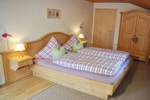 A wooden bed with a plaid bedspread, two nightstands with lamps, a wooden wardrobe, and a small framed picture on the wall. - Holiday apartment with 1 bedroom (Wallgau)