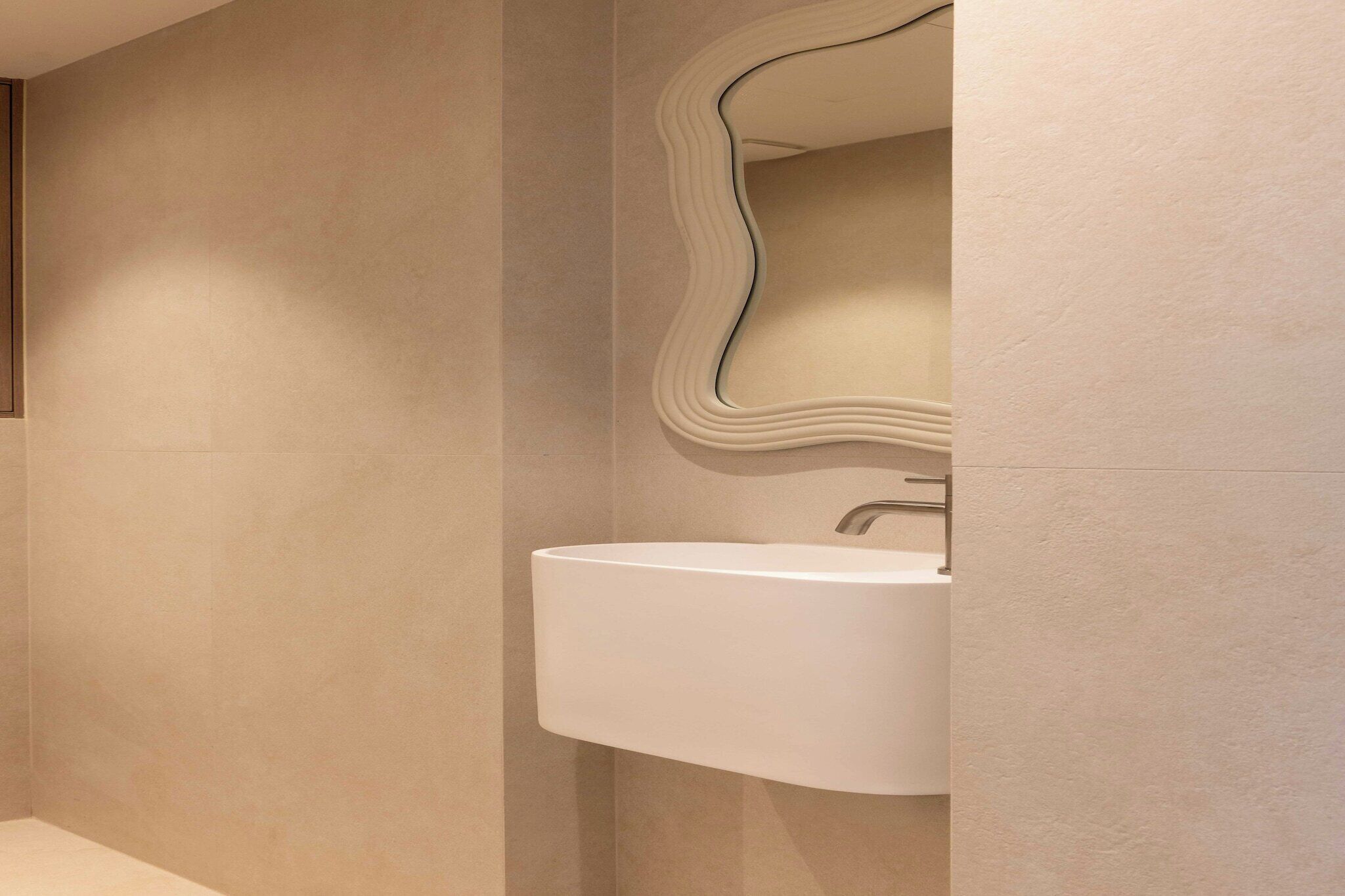 Un bagno moderno con uno specchio curvo, un lavandino bianco e una parete con finitura testurizzata.