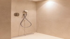 Una ducha moderna con cabezal de ducha de mano, panel de control en la pared y luz empotrada en el techo.