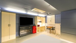 A compact room with a flat-screen TV, a red refrigerator, a dining table with chairs, and built-in cabinets. - 747 Motel (Gimcheon)