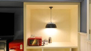 A kitchen with a microwave, kettle, and a red appliance on the counter, under a hanging light fixture. - 747 Motel (Gimcheon)