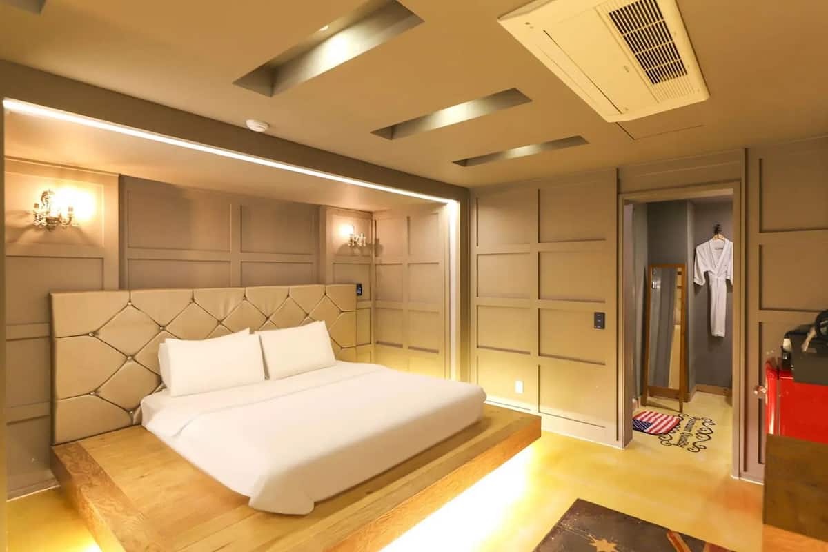 A modern hotel room with a large bed, a vanity with a mirror, and a red desk.