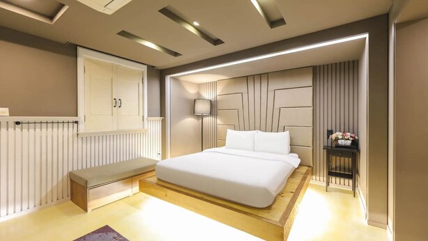 A modern bedroom with a bed, bench, bedside table, lamp, and a radiator. - 747 Motel (Gimcheon)