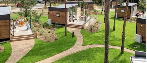 A modern outdoor area with wooden cabins, a paved walkway, and a grassy lawn.