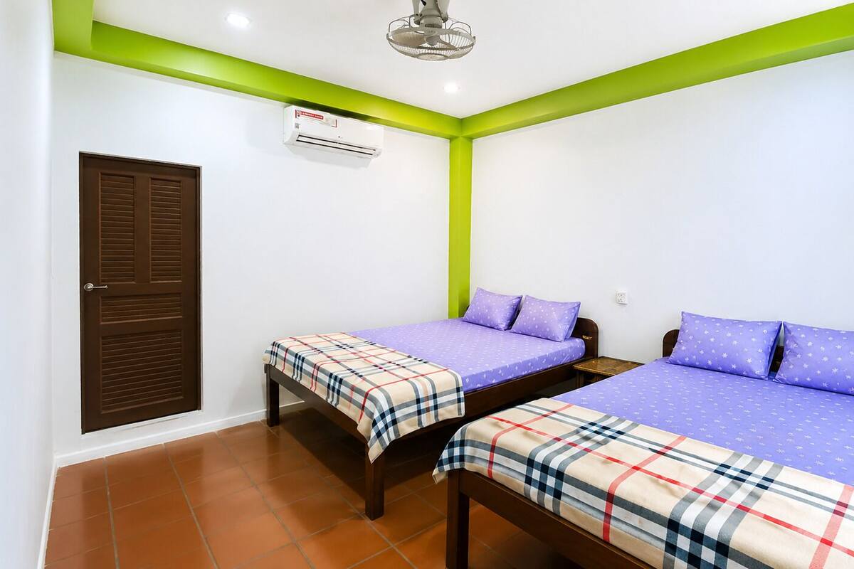 Ein Zimmer mit zwei Betten, einer braunen Tür, einer Klimaanlage und einer Wand in Grünton.