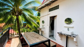 A balcony with a wooden table, a white sink with a tiled countertop, and a door leading to a bathroom.