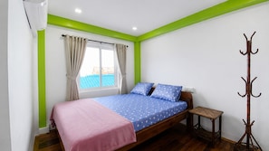 A bedroom with a bed, a window with curtains, a coat rack, and a bedside table. - Villa Koh Rong & Dormitory (Koh Rong)