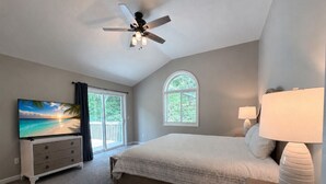 Un dormitorio con cama, ventilador de techo, televisión, cómoda y ventana.