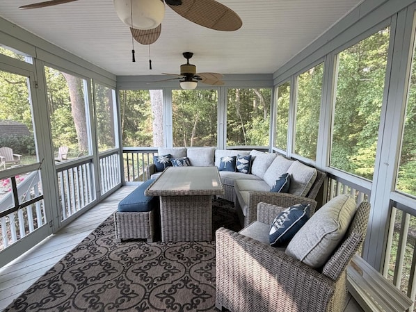 A covered porch with a table and chairs, large windows, and a ceiling fan.
