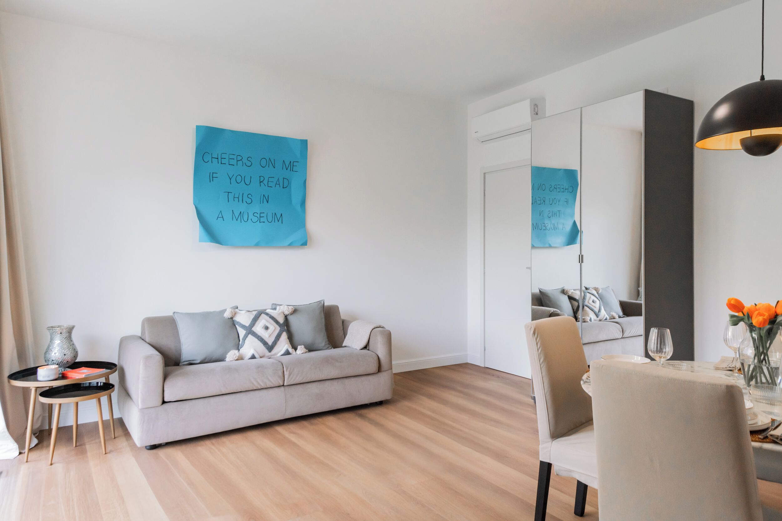A modern living room with a sofa, a dining table, and a large mirror.