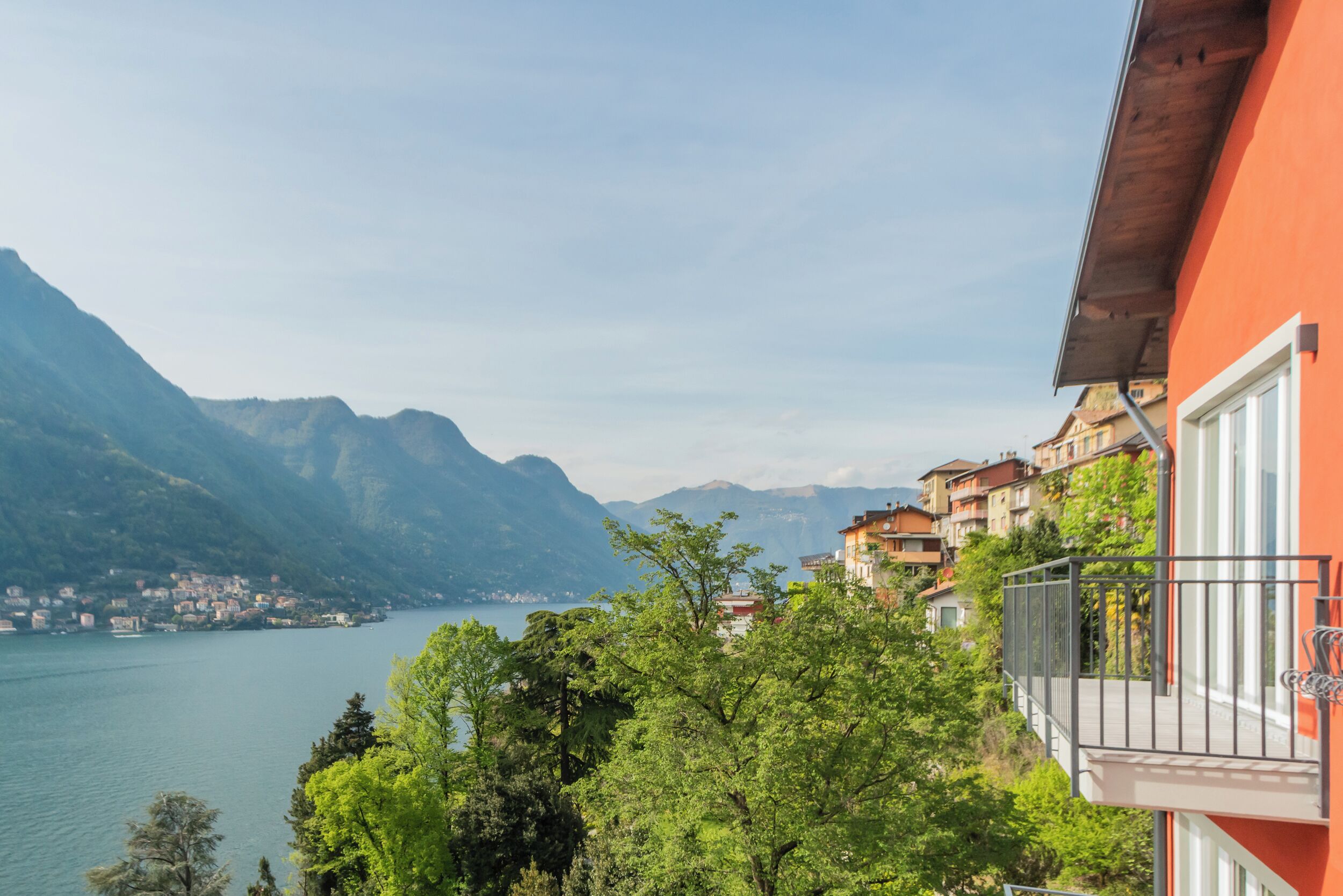 Vista de montaña con un lago, un edificio rojo con balcones y un pueblo al fondo.