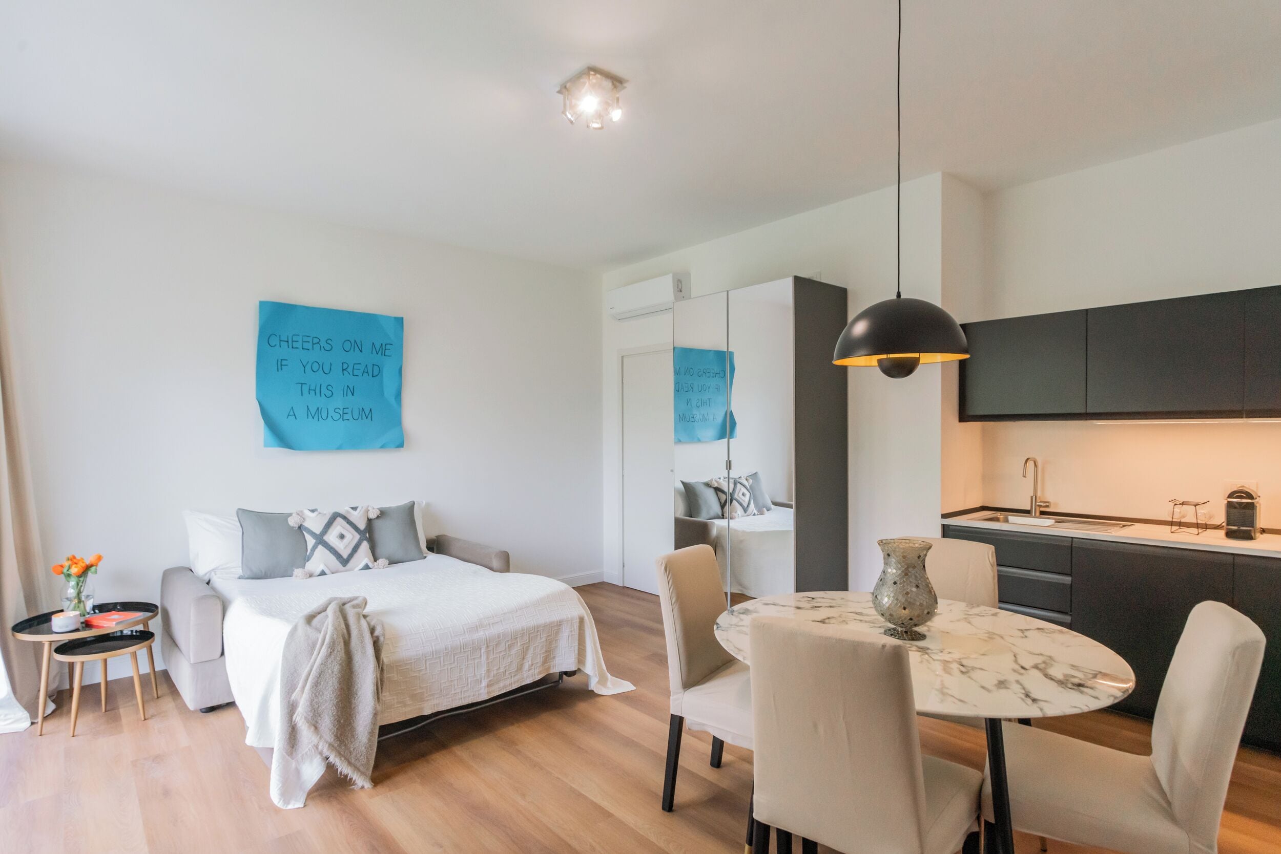 Una habitación de hotel moderna con cama, mesita de noche, silla y una pequeña mesa de comedor con sillas.
