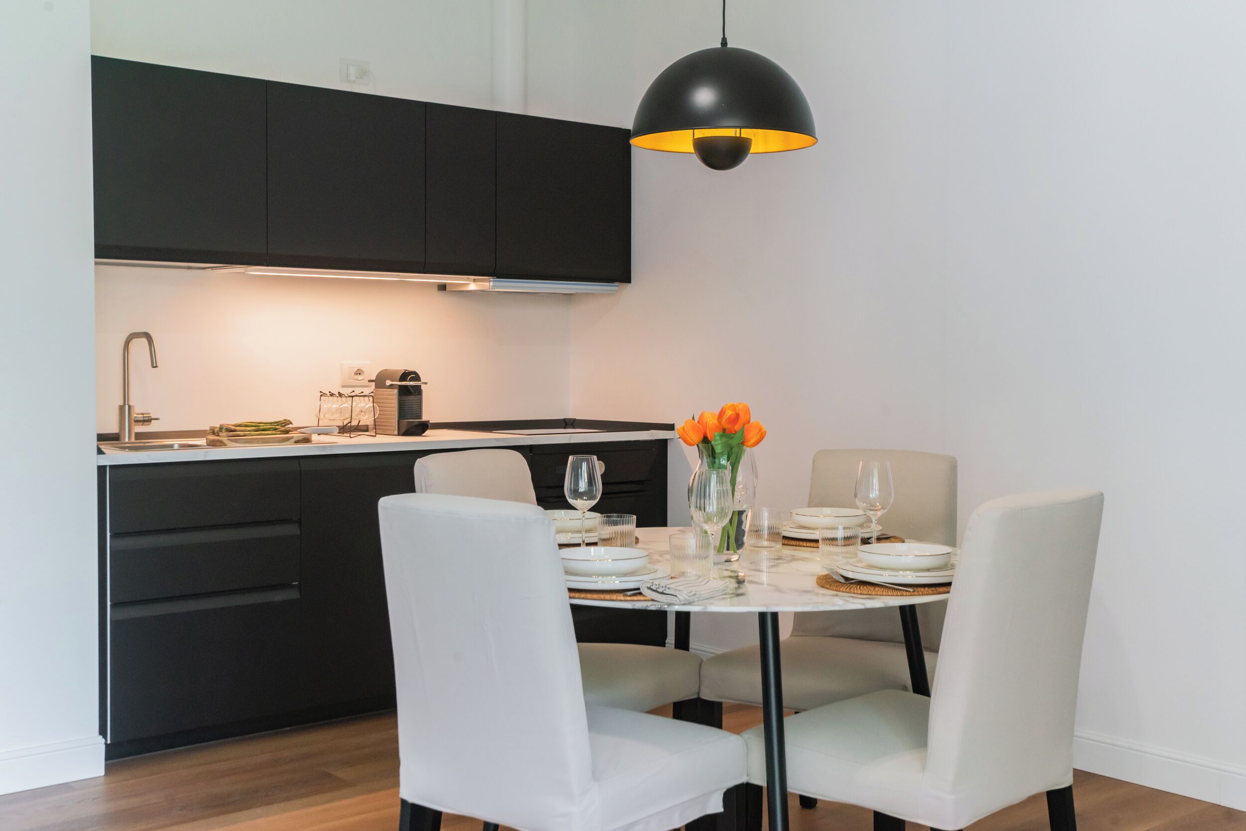 Cozinha moderna com armários pretos, uma mesa de jantar branca e uma luminária pendente.