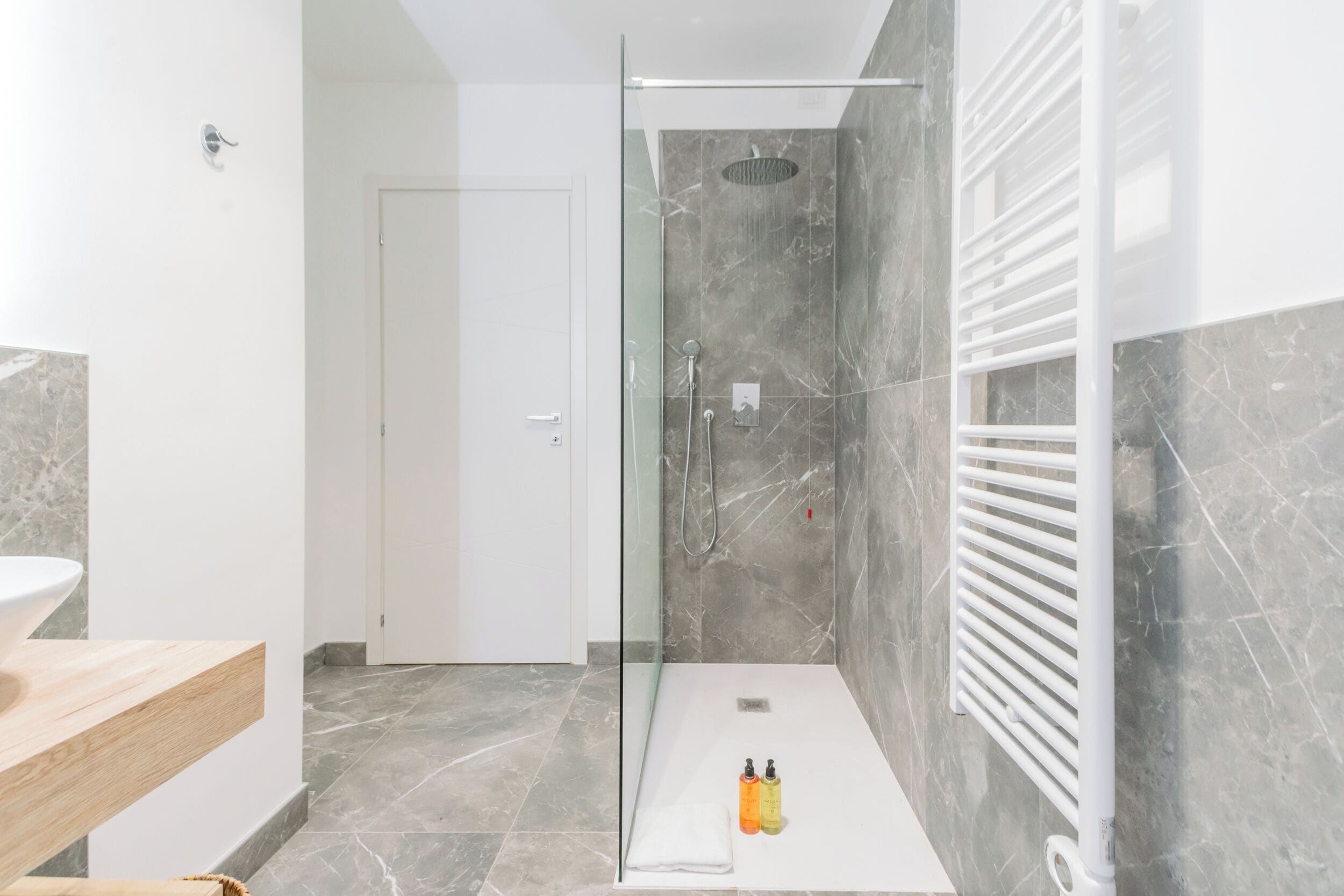 A modern bathroom with a glass-enclosed shower, marble walls, a white sink, and a towel rack.