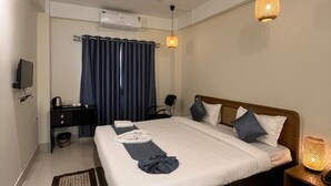 A hotel room with a bed, bedside table, ceiling fan, TV, and a desk with a chair. - The Happy Nest- A Boutique stay only 5 mins from Assam State Zoo (Guwahati)