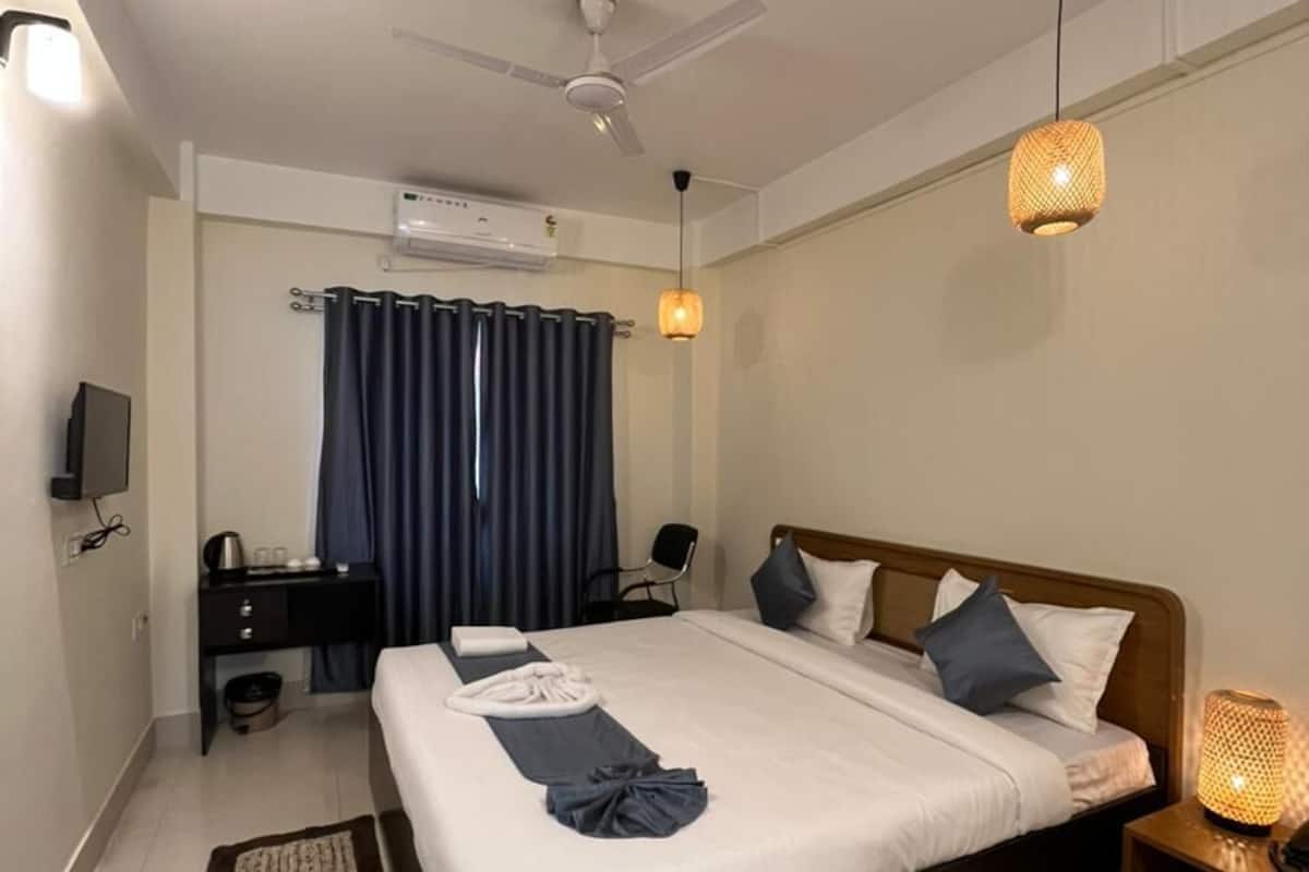 A hotel room with a bed, bedside table, ceiling fan, TV, and a desk with a chair.