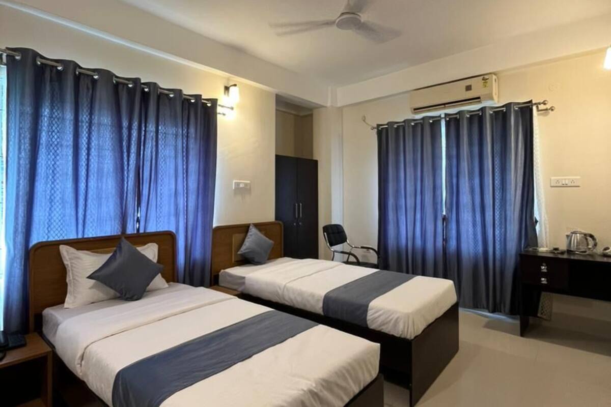 A hotel room with two beds, a ceiling fan, an air conditioning unit, a desk, and a chair.