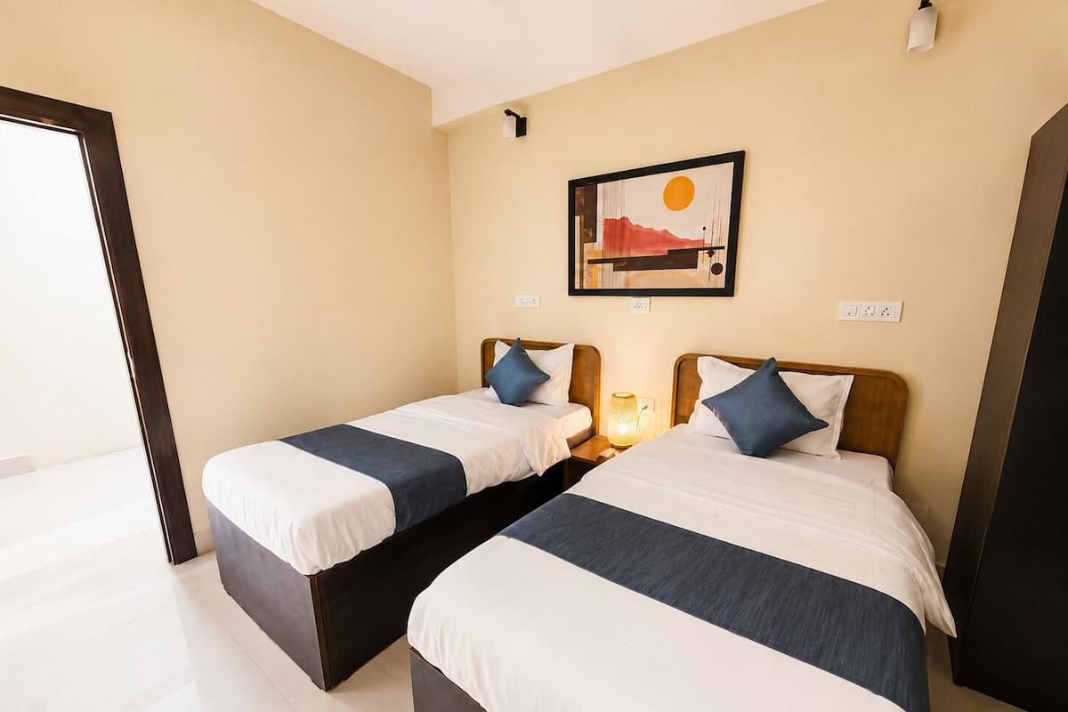 A hotel room with two beds, a painting on the wall, and a door leading to the outside.