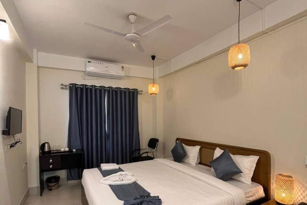 A modern hotel room with a bed, a desk, a chair, a TV, and a ceiling fan.