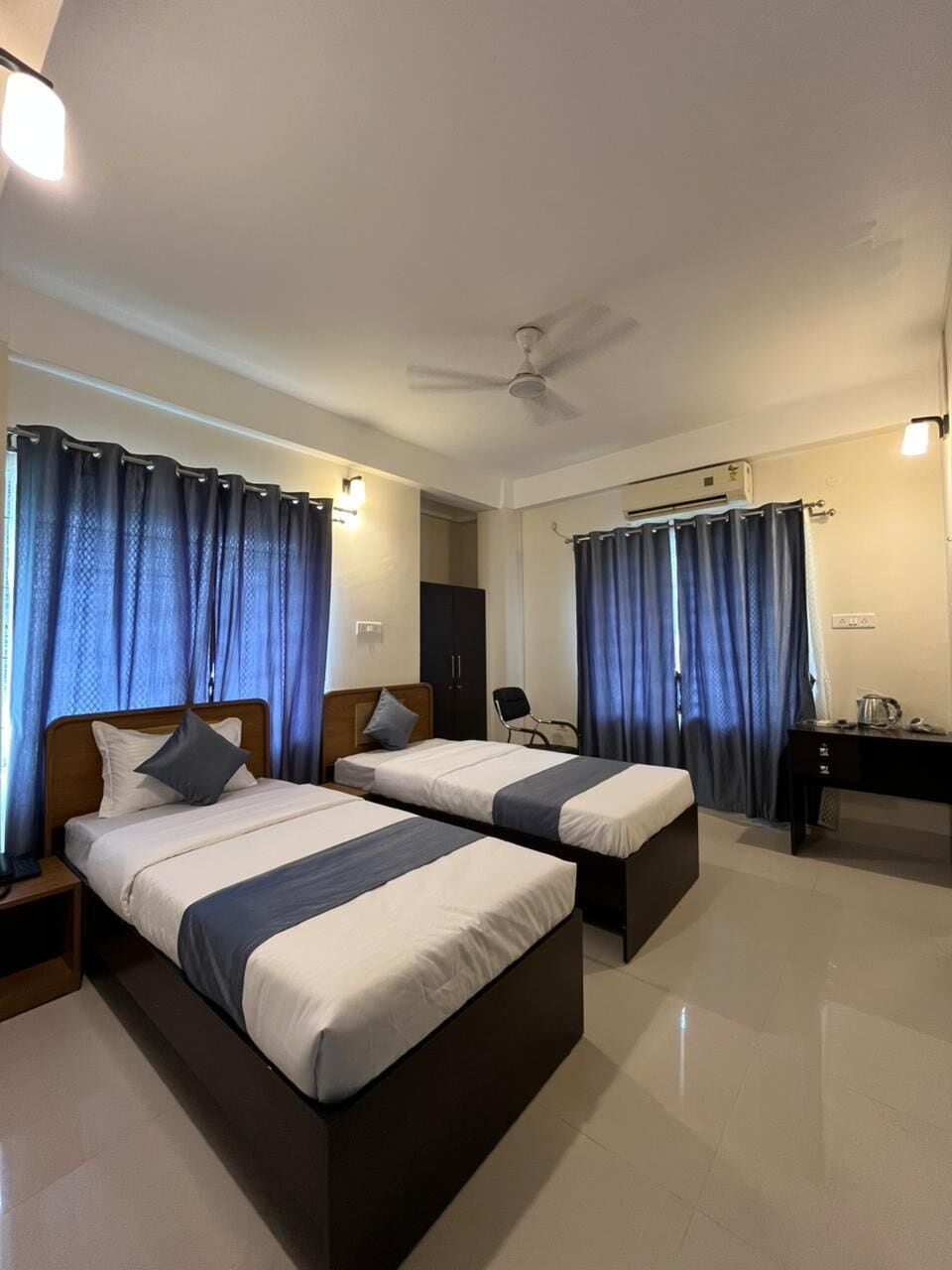 A hotel room with two beds, a desk, a chair, a ceiling fan, and curtains.