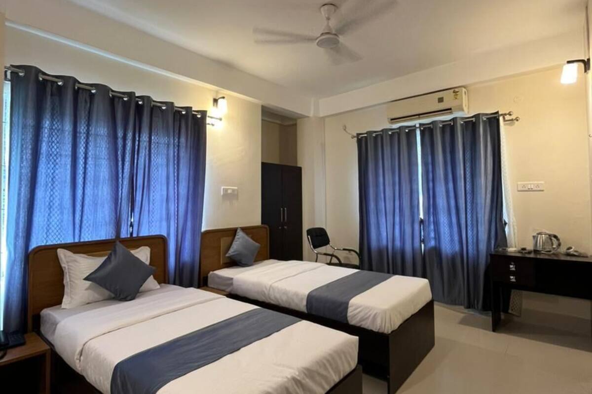 A hotel room with two beds, a desk, a chair, a ceiling fan, and curtains.