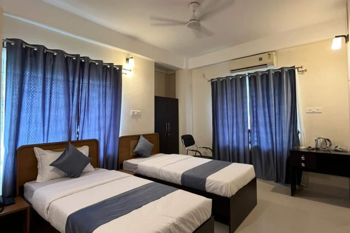 Habitación de hotel con dos camas, un escritorio, una silla, un ventilador de techo y cortinas.