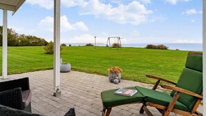 Un patio con una poltrona imbottita verde, un'altalena e vista sul mare.
