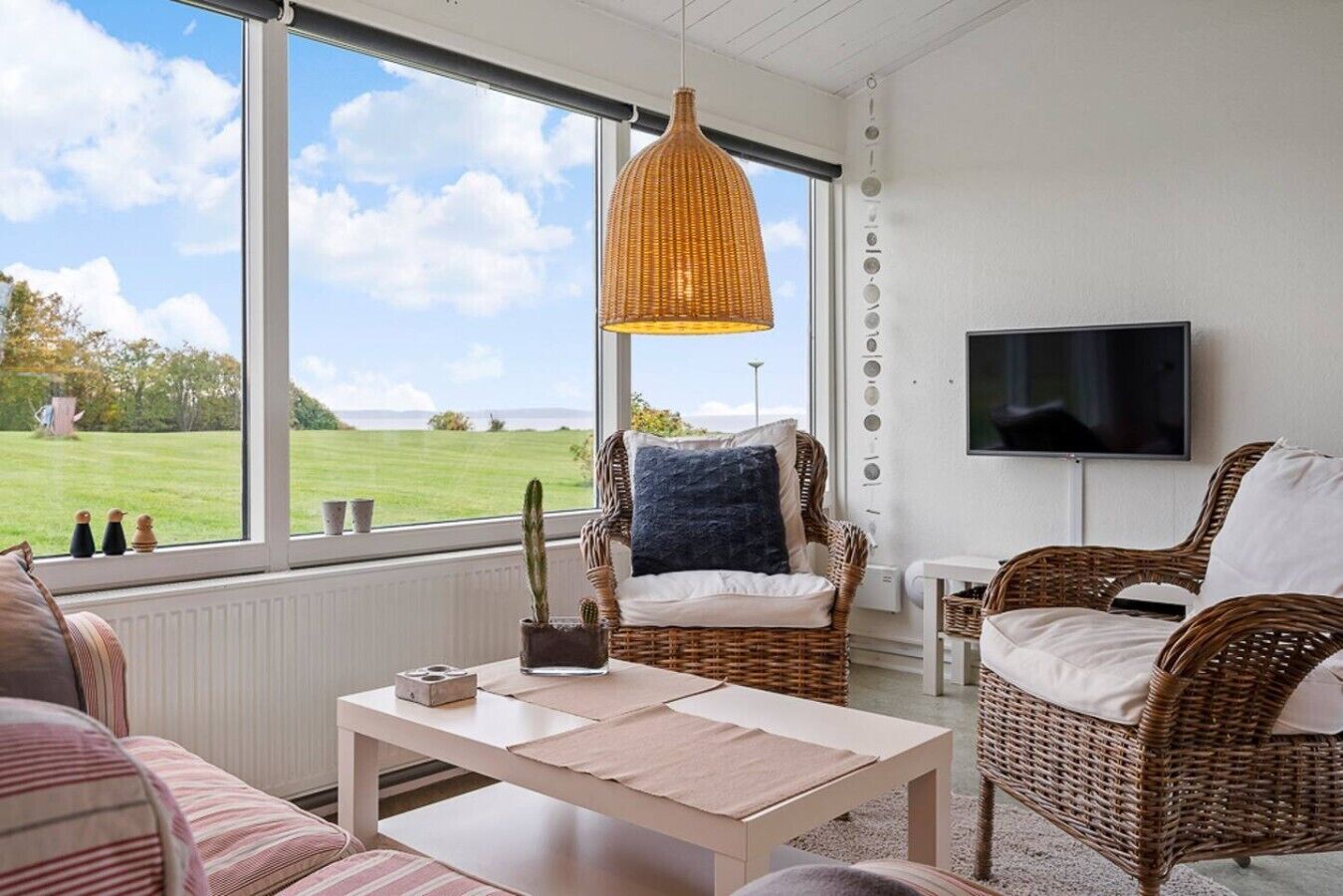 A room with wicker furniture, a television, and a view of a grassy field.