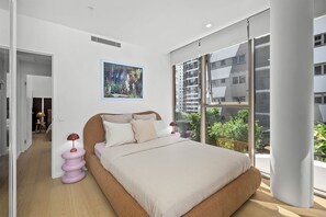 Ein modernes Schlafzimmer mit einem großen Bett, einem Gemälde und Blick auf ein Gebäude durch ein großes Fenster.