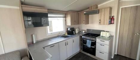 A compact kitchen with a microwave, stove, and sink, wooden cabinets, and a window.