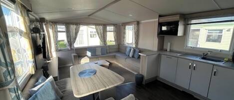 A compact RV interior with a dining area, sofa, kitchenette, and a TV.