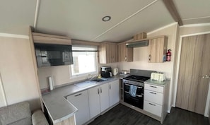 A compact kitchen with a microwave, stove, sink, and cabinets. - Modern 3-bedroom Caravan Near Beach at T (Abergele)