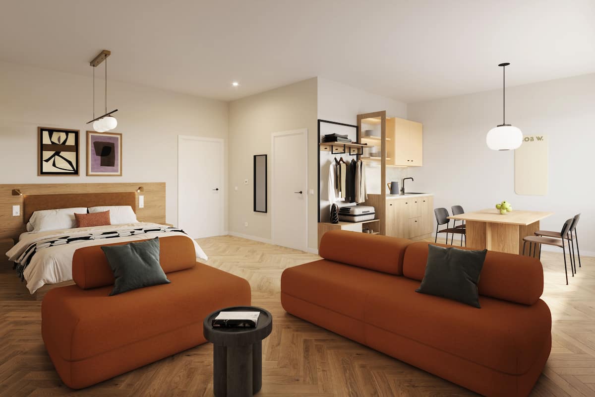 A modern hotel room with a bed, two sofas, a small table, a desk, and a kitchenette.