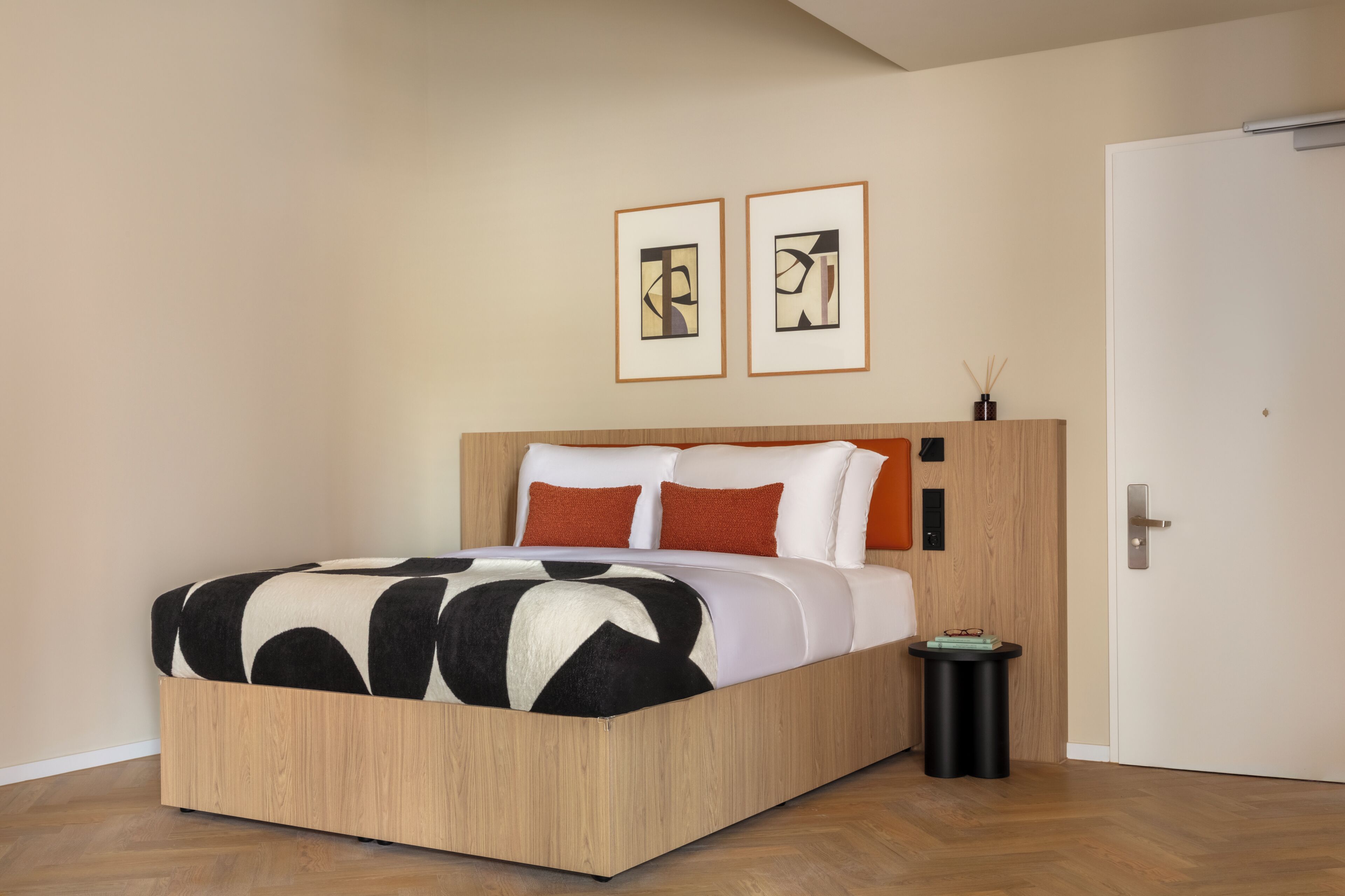 A modern bedroom with a wooden bed frame, white bedding, and two abstract paintings on the wall.