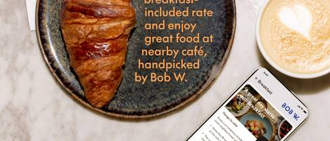 A croissant on a plate with a cup of coffee and a smartphone displaying a breakfast menu.