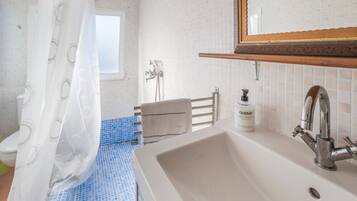 Un baño con lavamanos blanco, espejo, cortina de ducha, toallero y ventana.