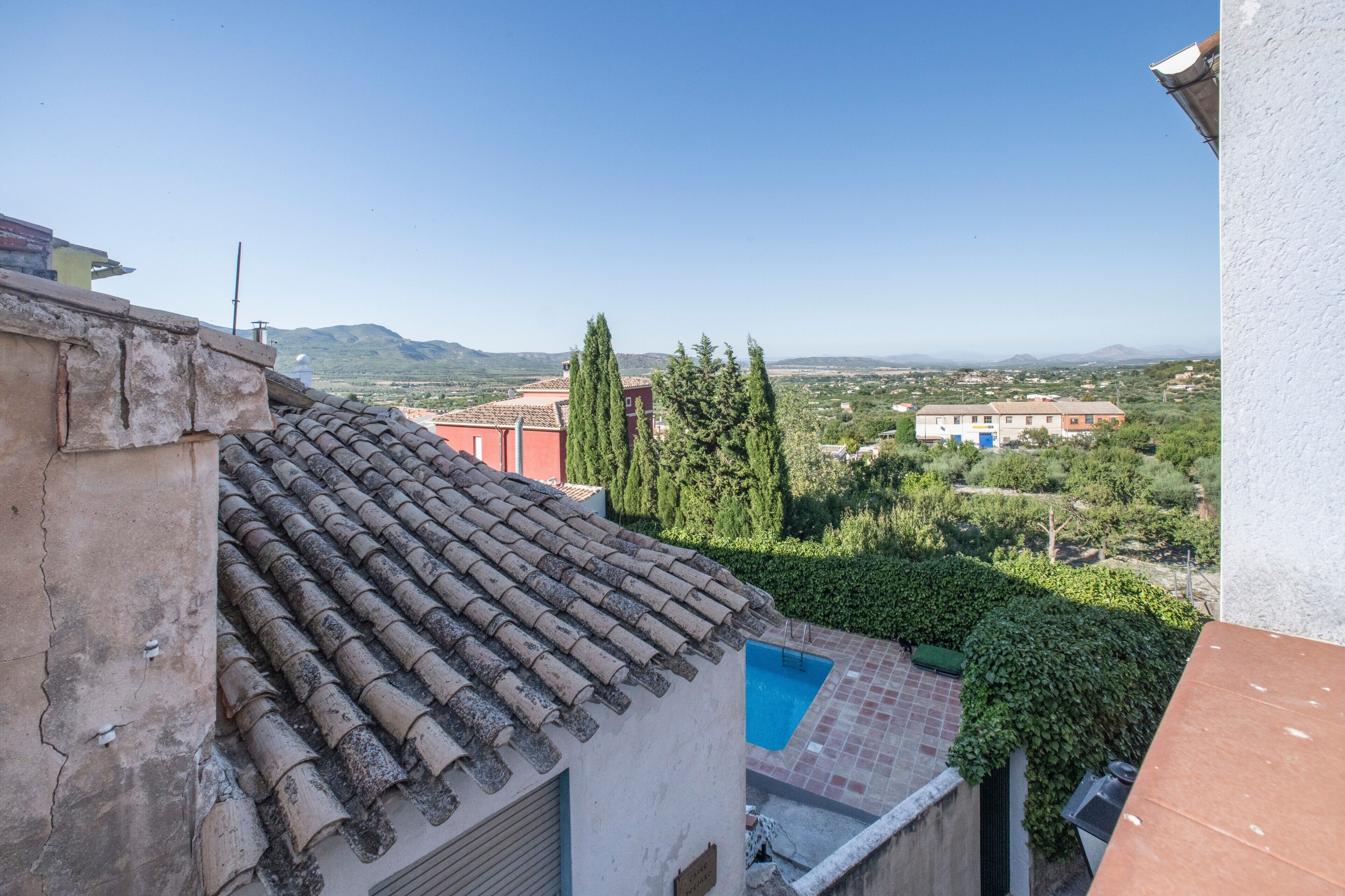 Una terraza con piscina, vistas del paisaje circundante y un edificio con tejado de tejas.