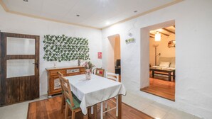Un comedor con una mesa de madera, sillas, mantel blanco, pared decorativa y una puerta.