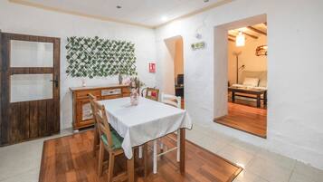 Un comedor con una mesa de madera, sillas, mantel blanco, pared decorativa y una puerta.