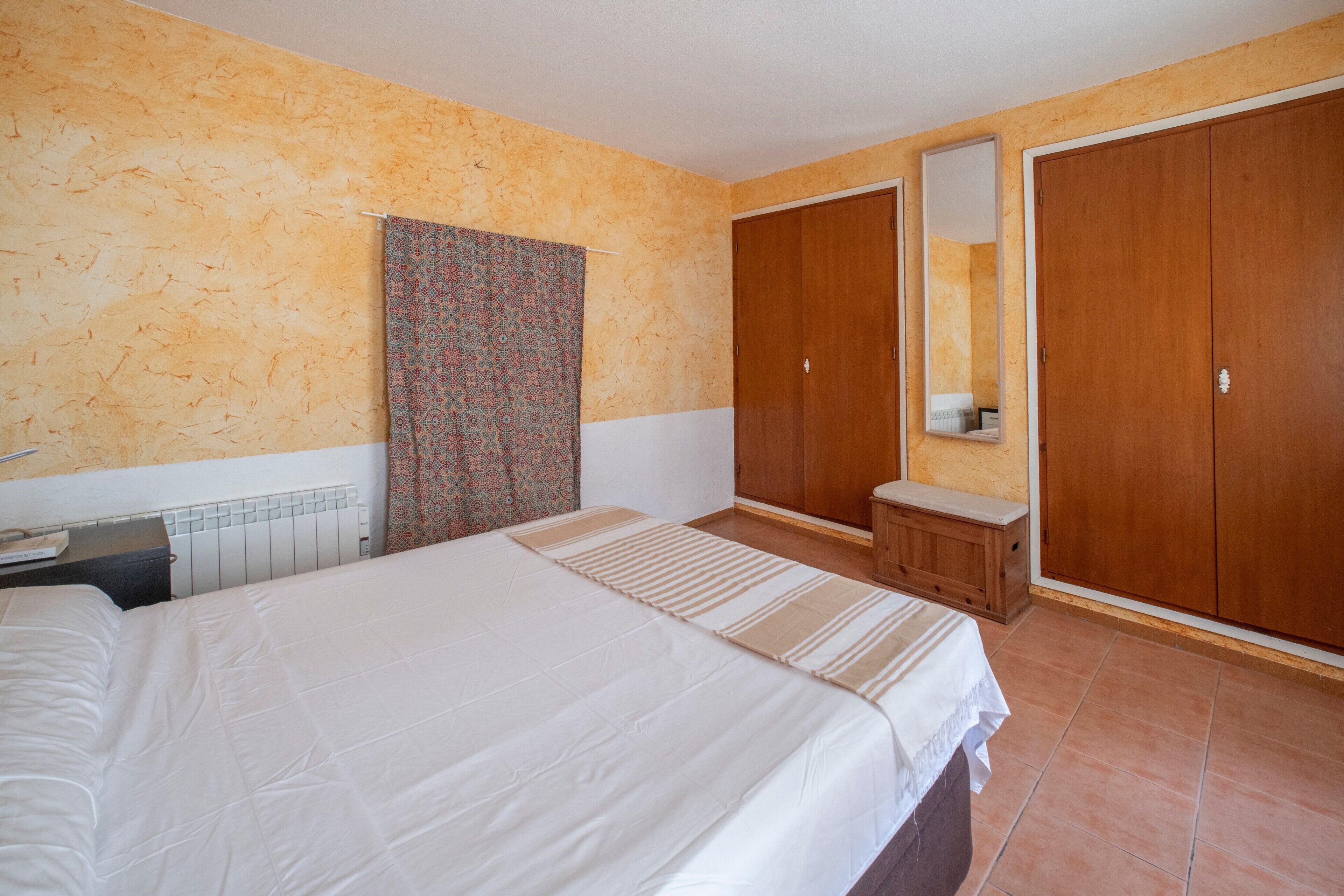 A bedroom with a bed, a nightstand, a dresser, a mirror, and a wardrobe.