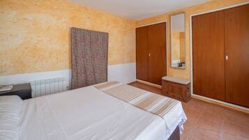 A bedroom with a bed, a nightstand, a dresser, a mirror, and a wardrobe.