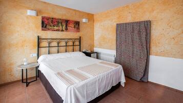 Un dormitorio con cama, mesita de noche, lámpara de pared, radiador y cortina estampada.