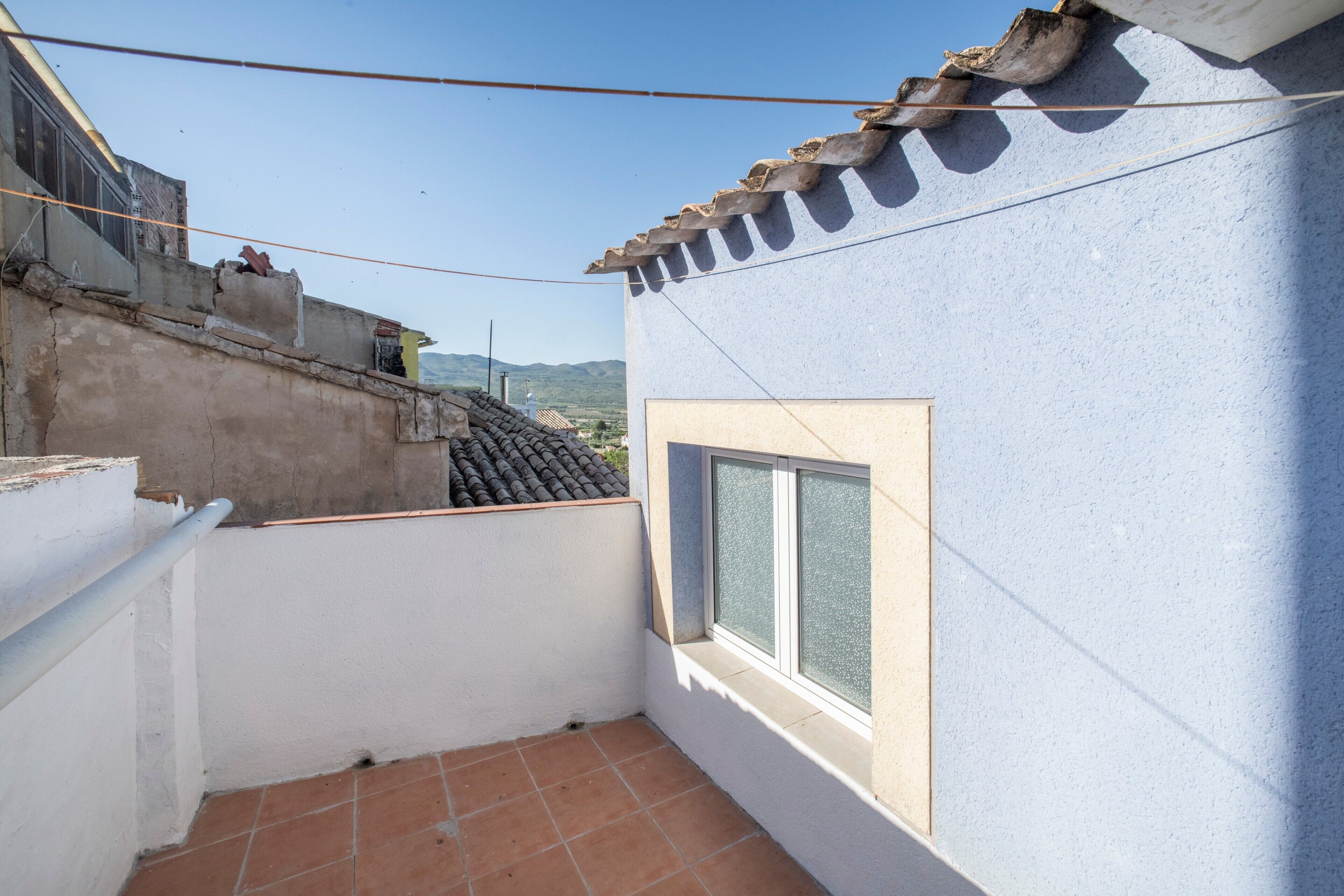 Un petit balcon doté d’un sol carrelé, d’une fenêtre et offrant une vue sur les bâtiments environnants.