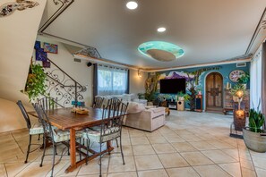 Uma sala de estar ampla com uma mesa de jantar de madeira, assentos confortáveis, uma TV de tela plana e plantas decorativas.