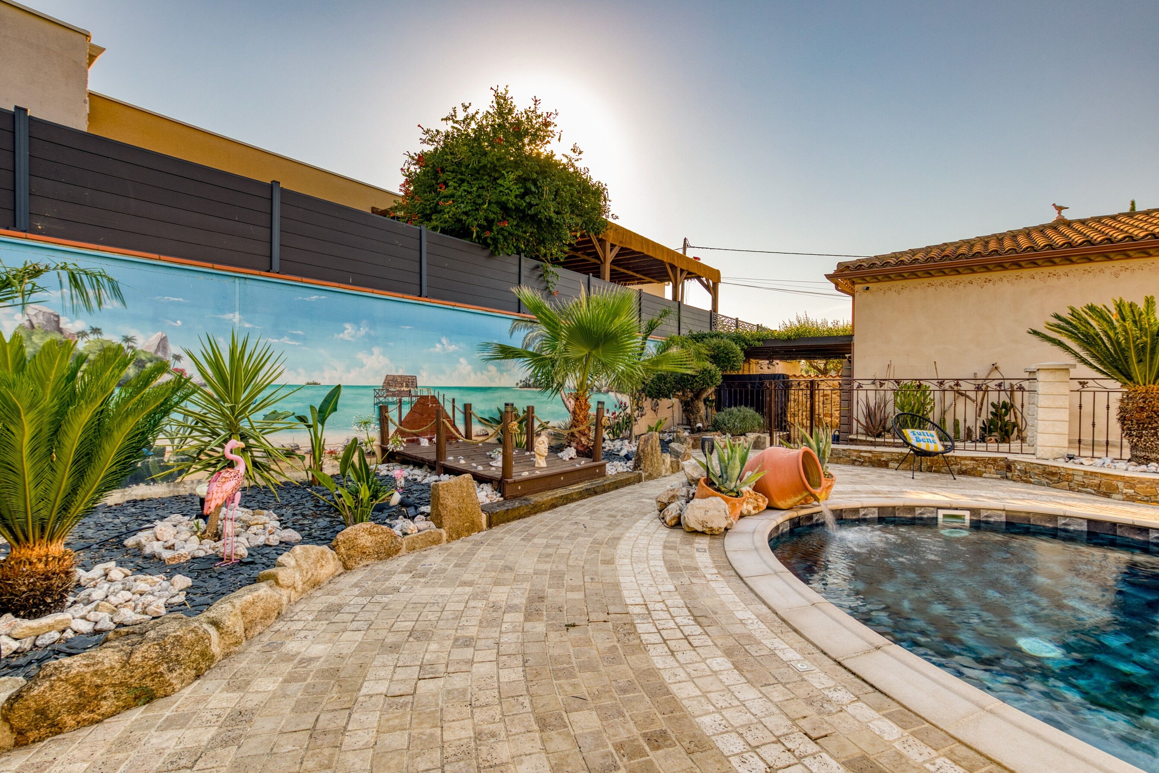 Piscina con un mural, una estatua de flamenco y un jardín tropical.